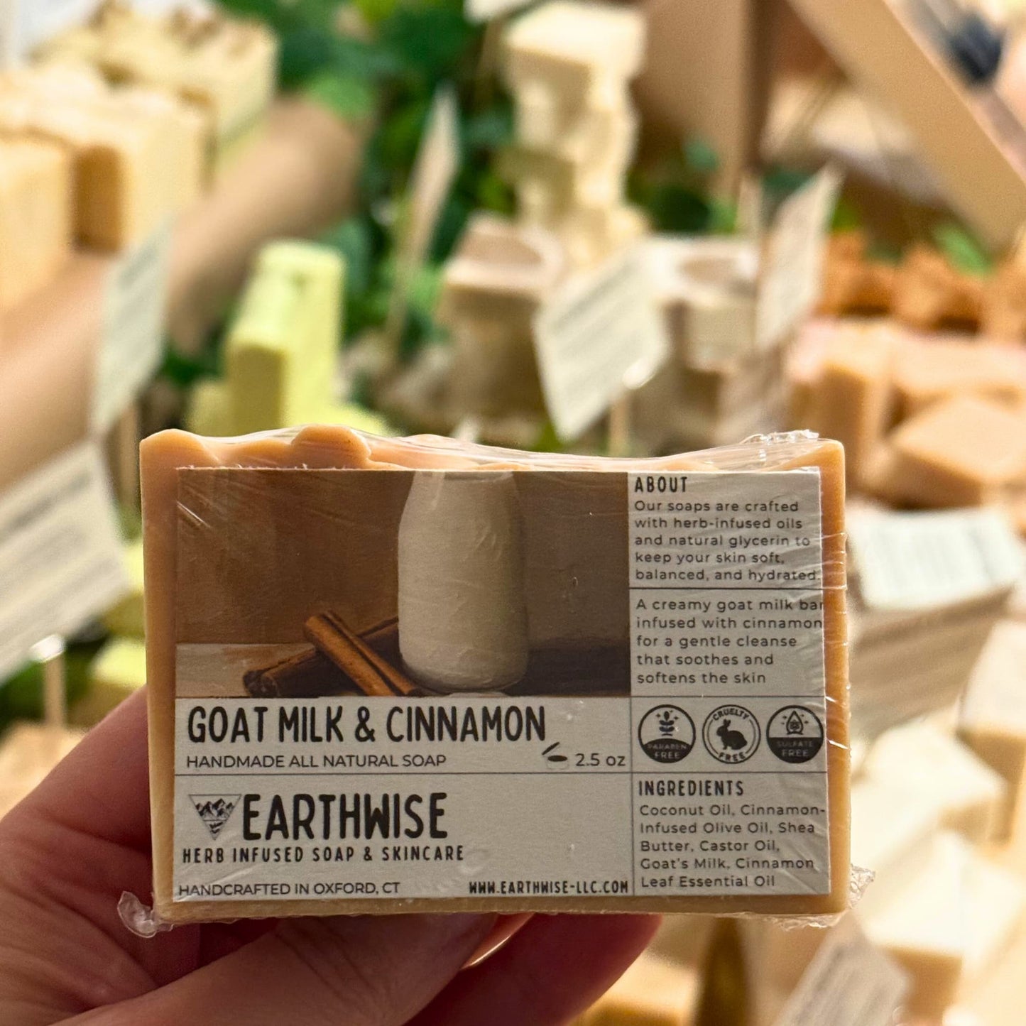 Handmade all natural soap bar with Earthwise branding held in a hand, with blurred background of more soaps.