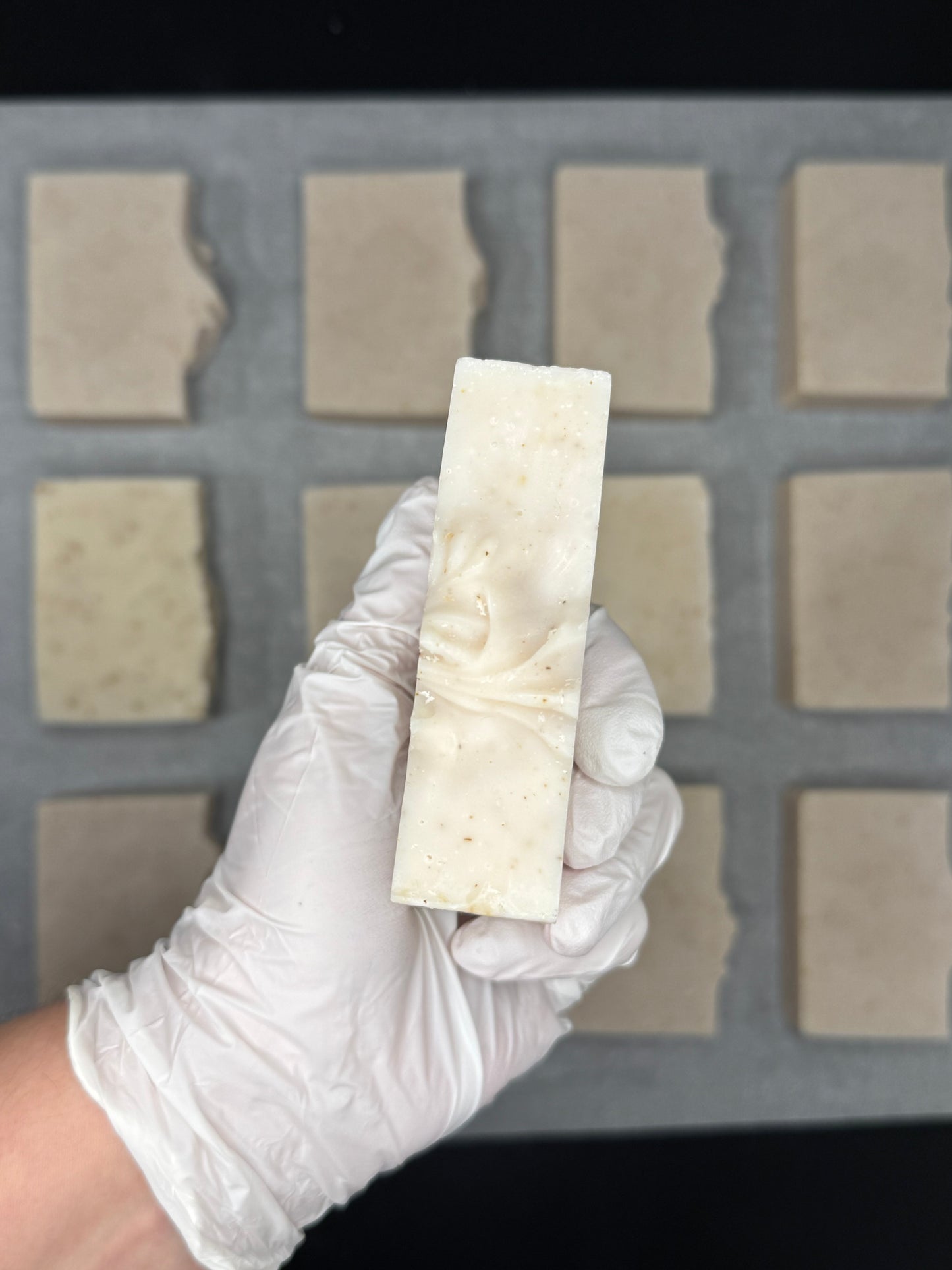 Hand wearing a white glove holding a rectangular bar of soap above a soap mold.