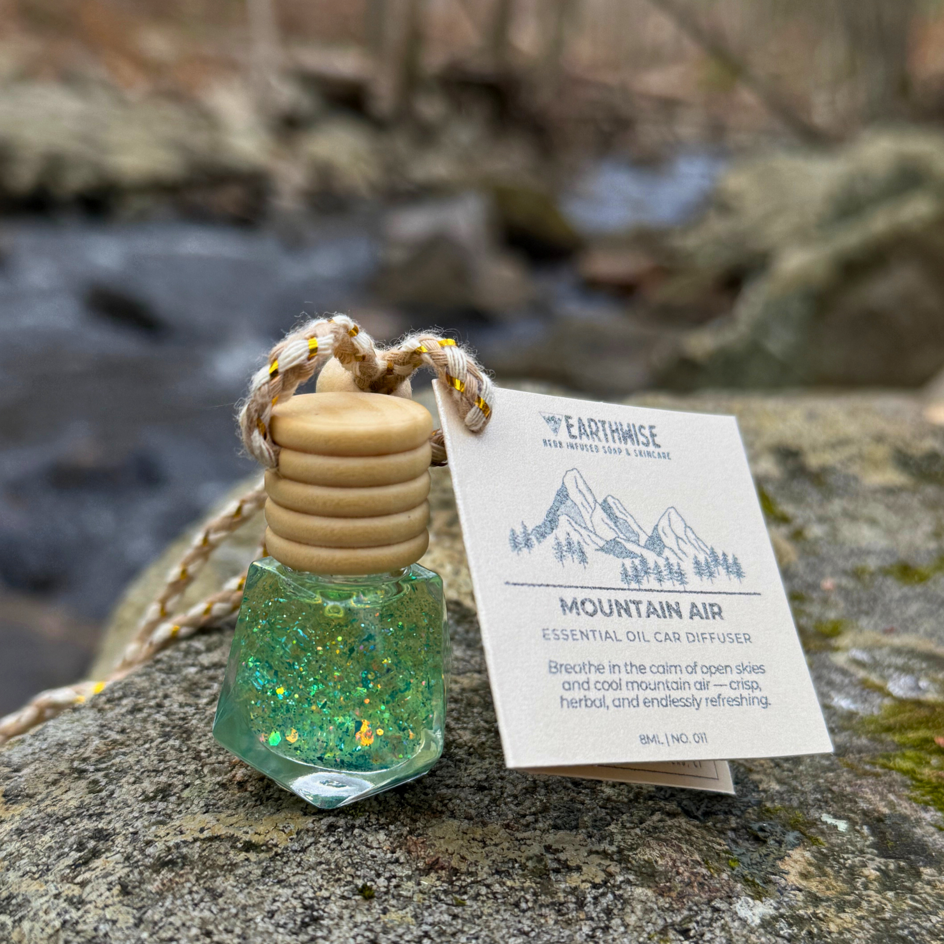 Essential oil diffuser with wooden top and green glittery base on a rock with a blurred natural background