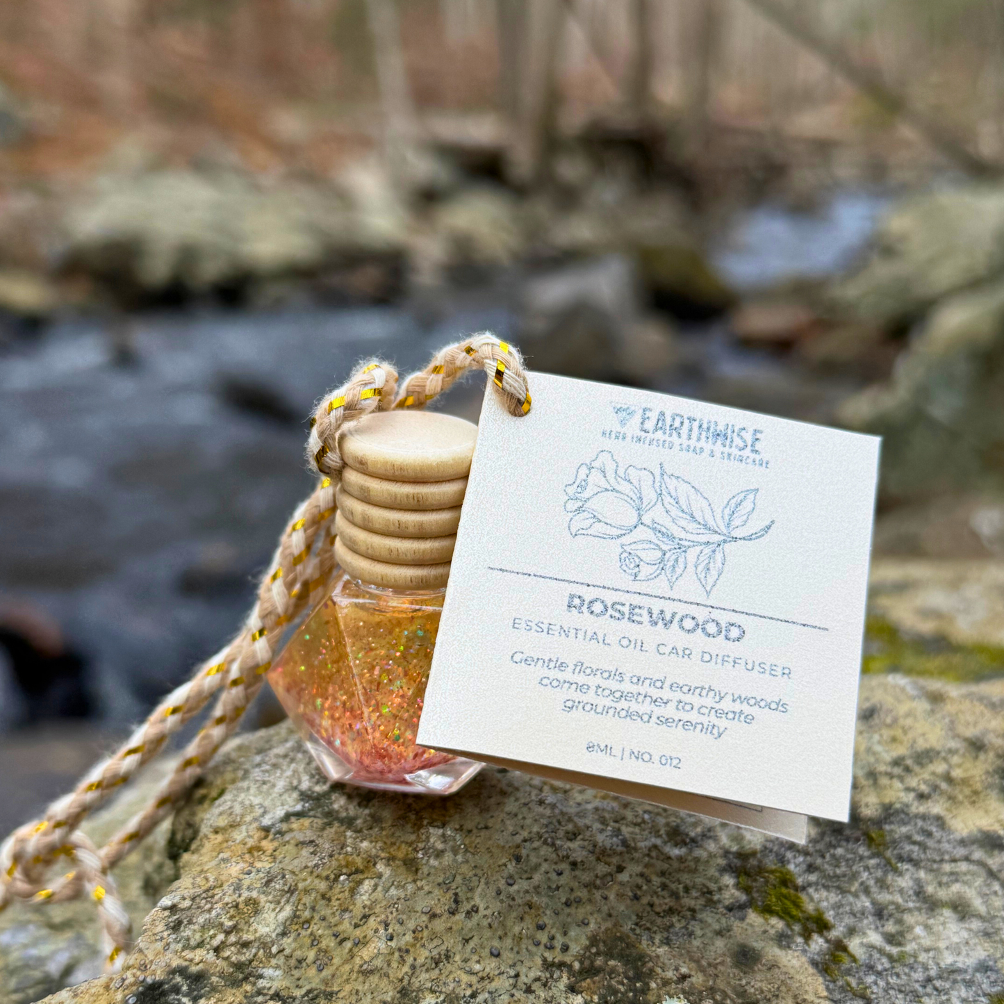Essential oil diffuser with wooden top on a rock by a stream, featuring Earthwise label.