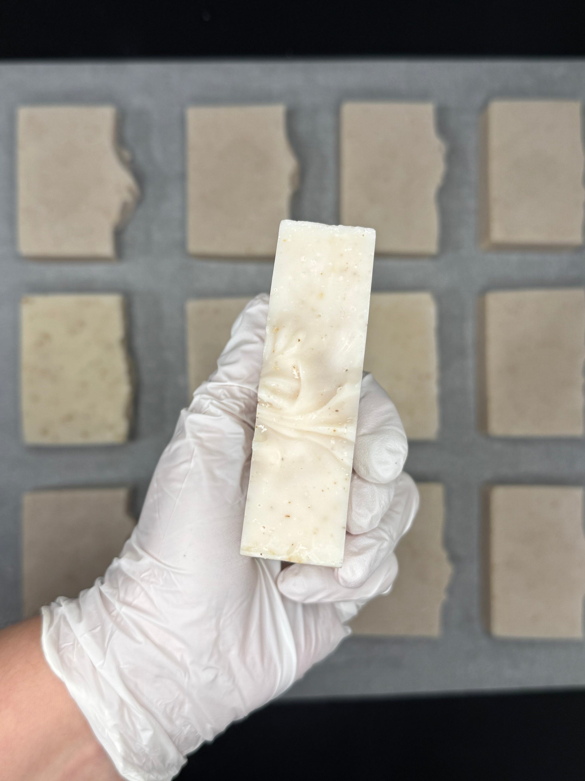 Hand wearing a white glove holding a rectangular bar of soap above a soap mold.