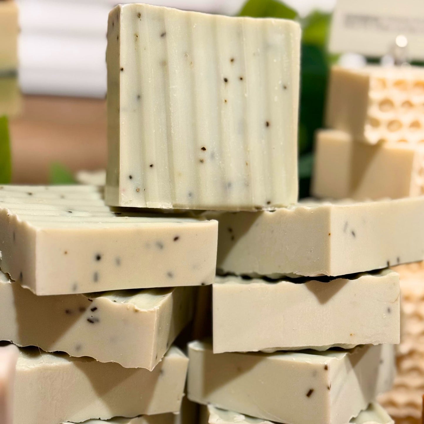 Stack of handmade rosemary soap bars with visible specks on a blurred natural background