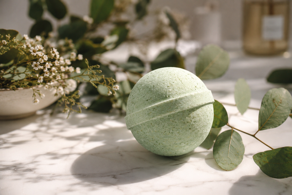 Green bath bomb on a marble surface with eucalyptus leaves and flowers in the background