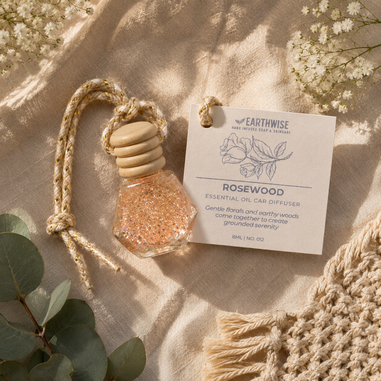 Earthwise Rosewood essential oil car diffuser with a tag on a textured surface with flowers and leaves.