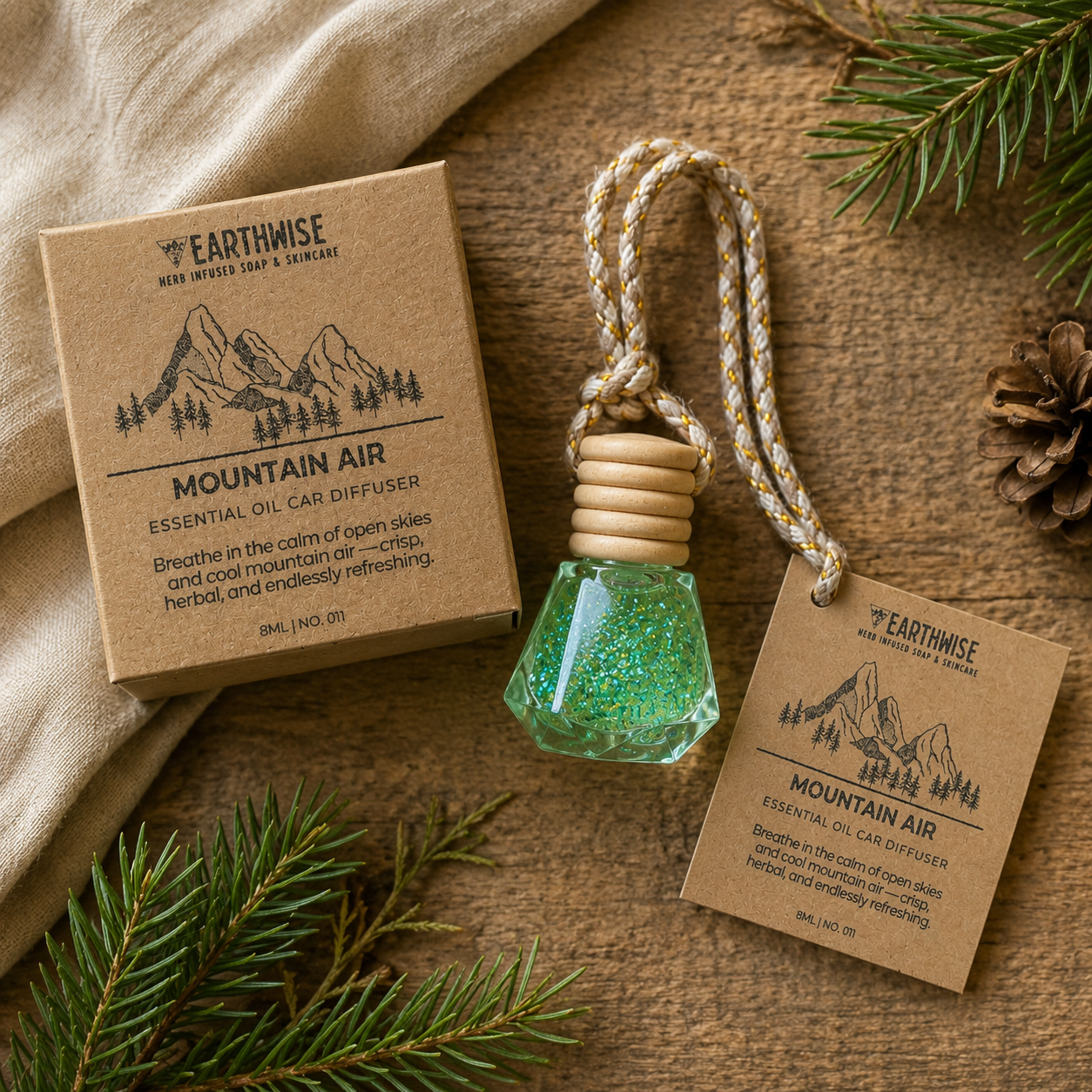 Earthwise Mountain Air essential oil car diffuser with packaging on a wooden surface with pine branches.