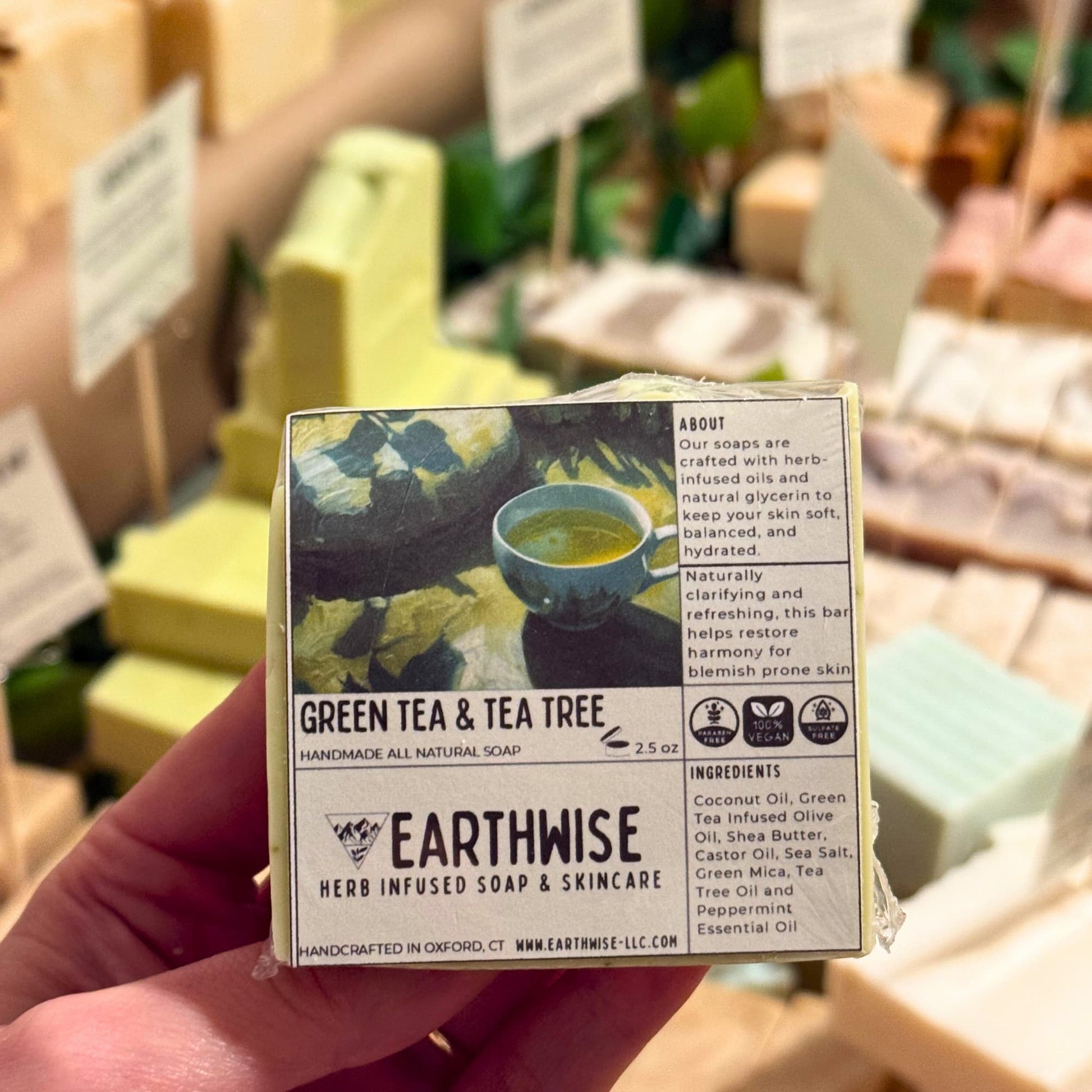 Hand holding a box of Earthwise Green Tea & Tea Tree soap with a blurred store background.