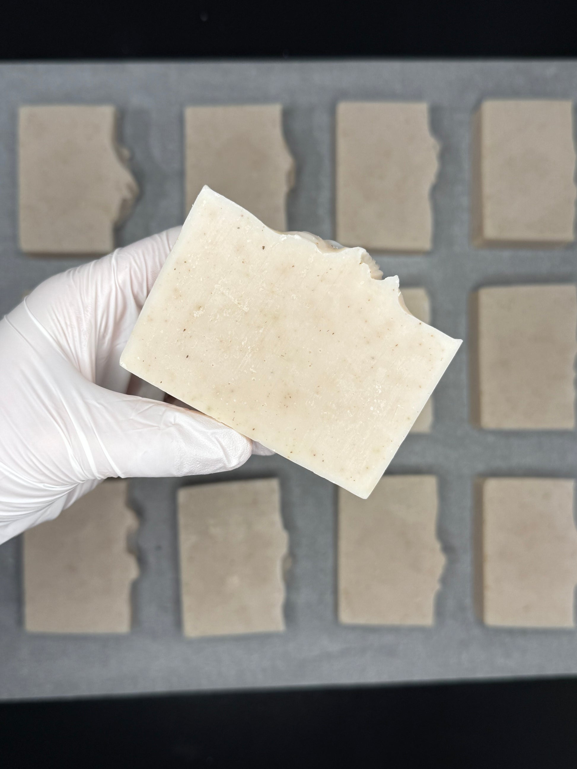 Hand wearing a white glove holding a square piece of beige material against a grid background.