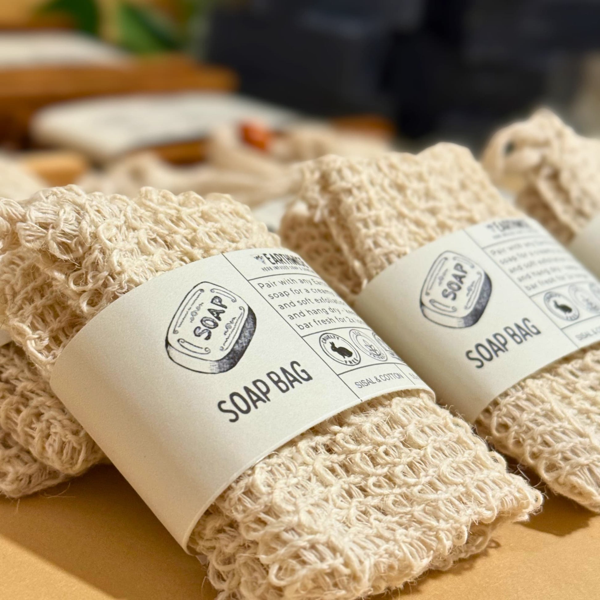 Two natural exfoliator beige soap bags with labels on a wooden surface