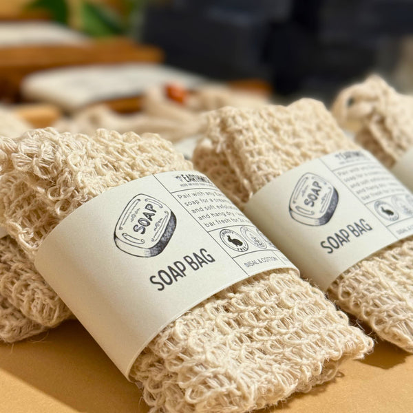 Two natural exfoliator beige soap bags with labels on a wooden surface