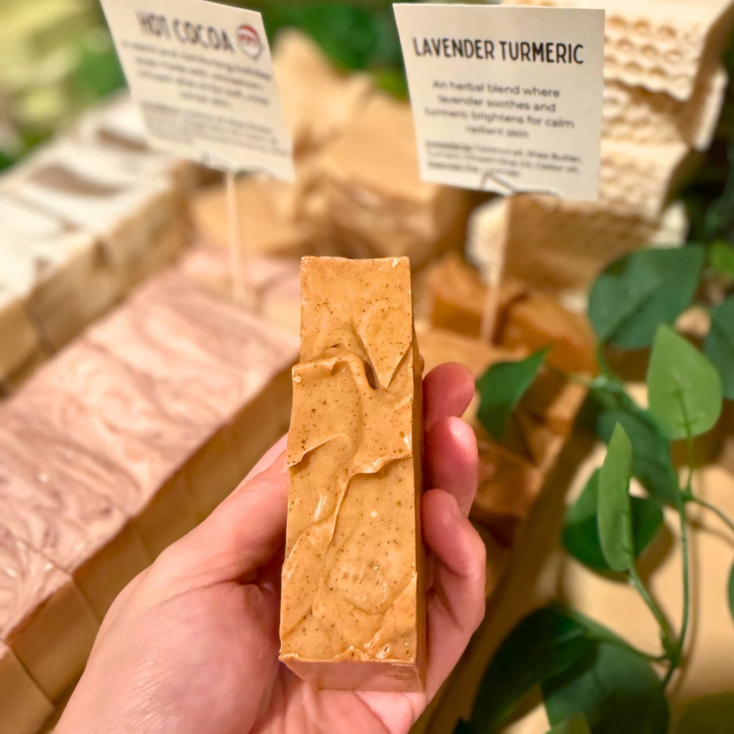 Hand holding a bar of soap with 'Lavender Turmeric' label in the background