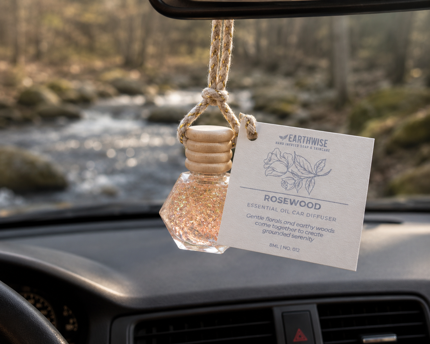 Car air freshener with 'Earthwise' label hanging from a car's rearview mirror with a scenic background.