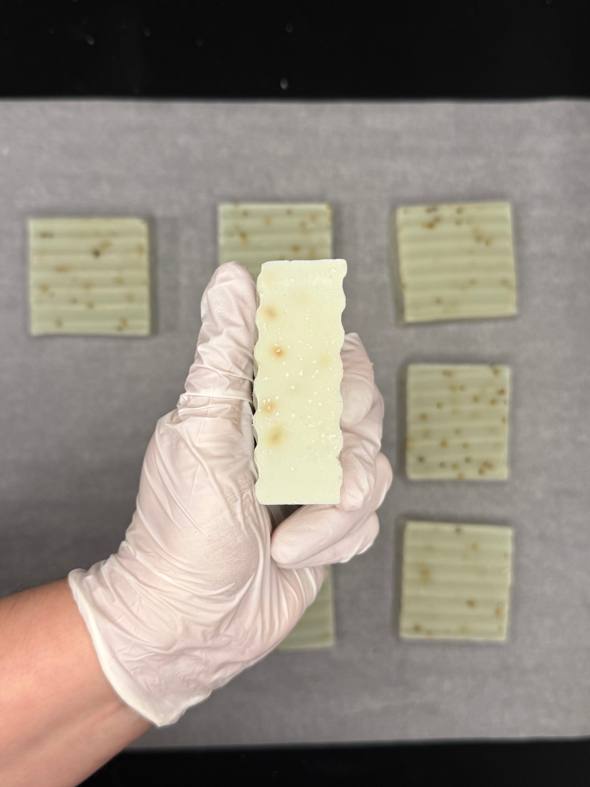 Hand wearing a white glove holding a bar of soap with a grid of soap bars in the background.