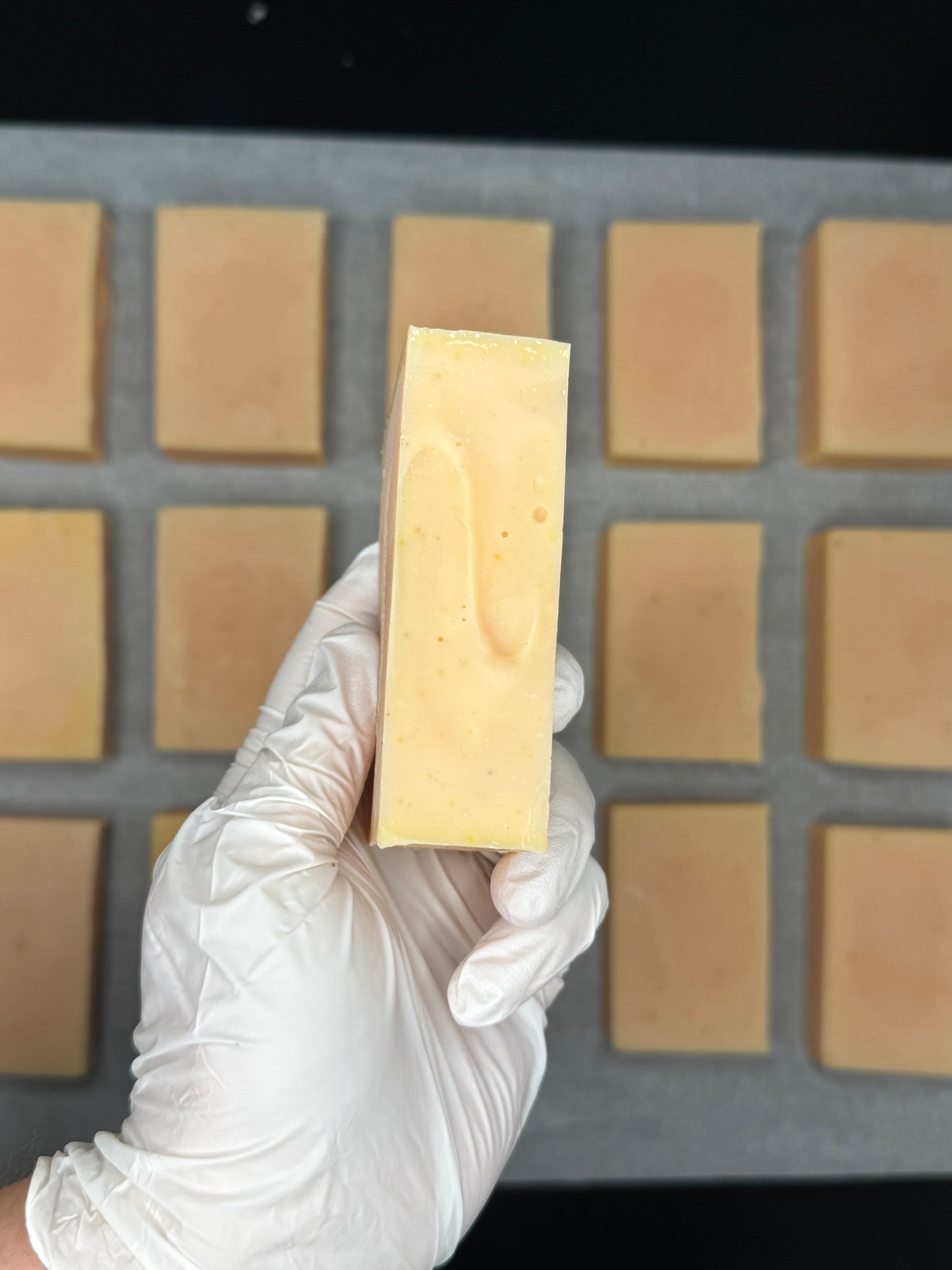 Hand holding a bar of soap above a soap mold with bars already cast.