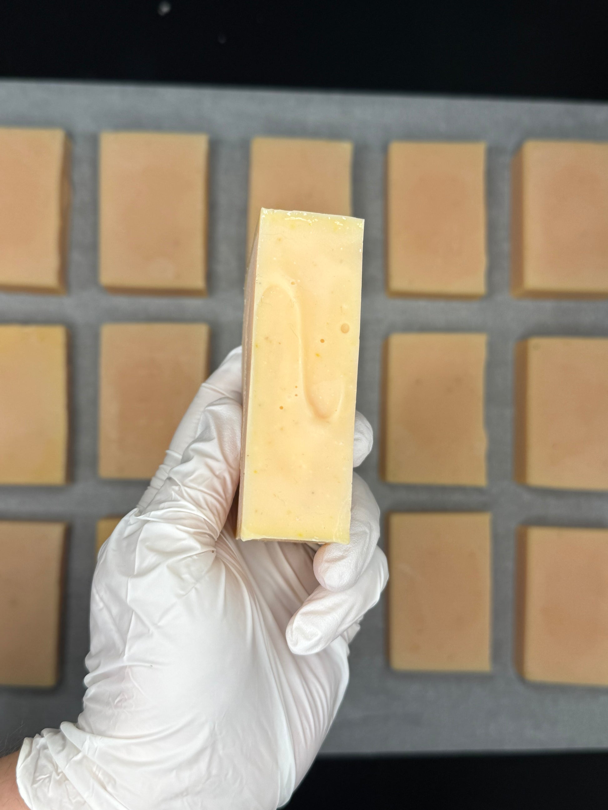 Hand holding a bar of soap above a soap mold with bars already cast.