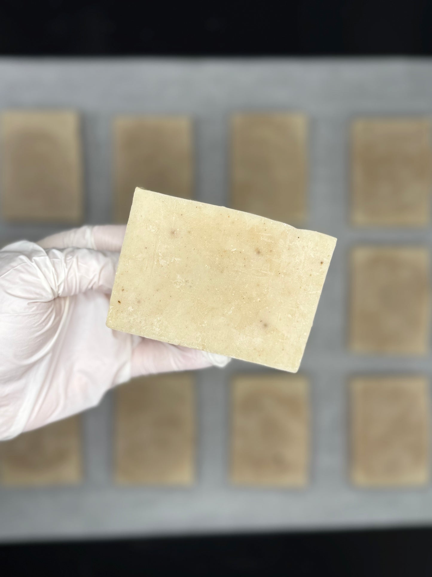 Hand wearing a glove holding a organic raspberry soap over a grid of similar pattern
