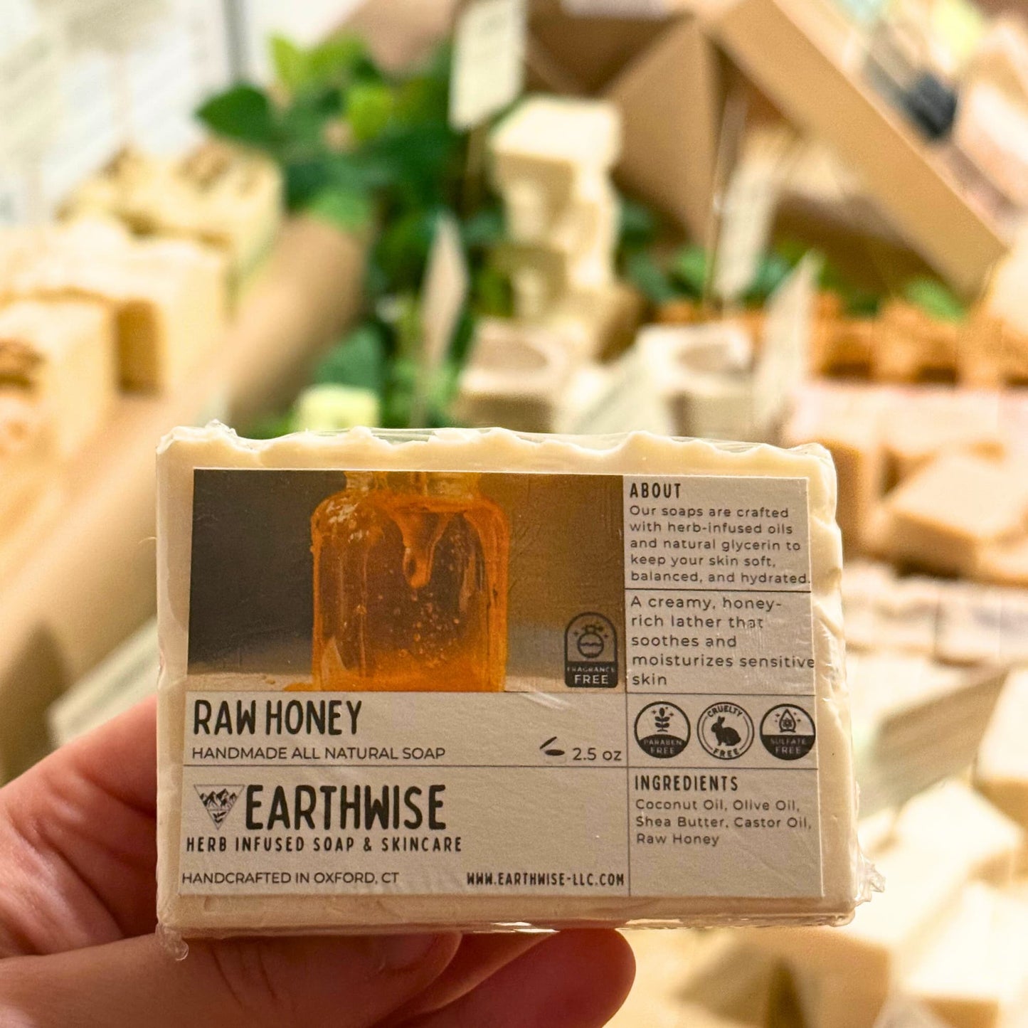 Handmade all natural soap bar labeled 'Raw Honey' by Earthwise held in a hand with a blurred background.