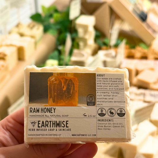 Handmade all natural soap bar labeled 'Raw Honey' by Earthwise held in a hand with a blurred background.