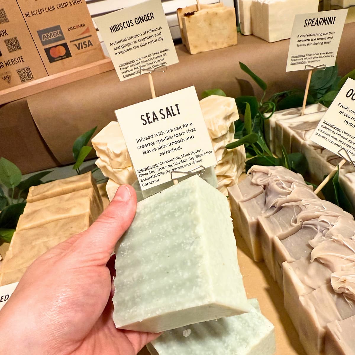 Hand holding a bar of Seasalt soap with other soap bars and product information cards in the background.