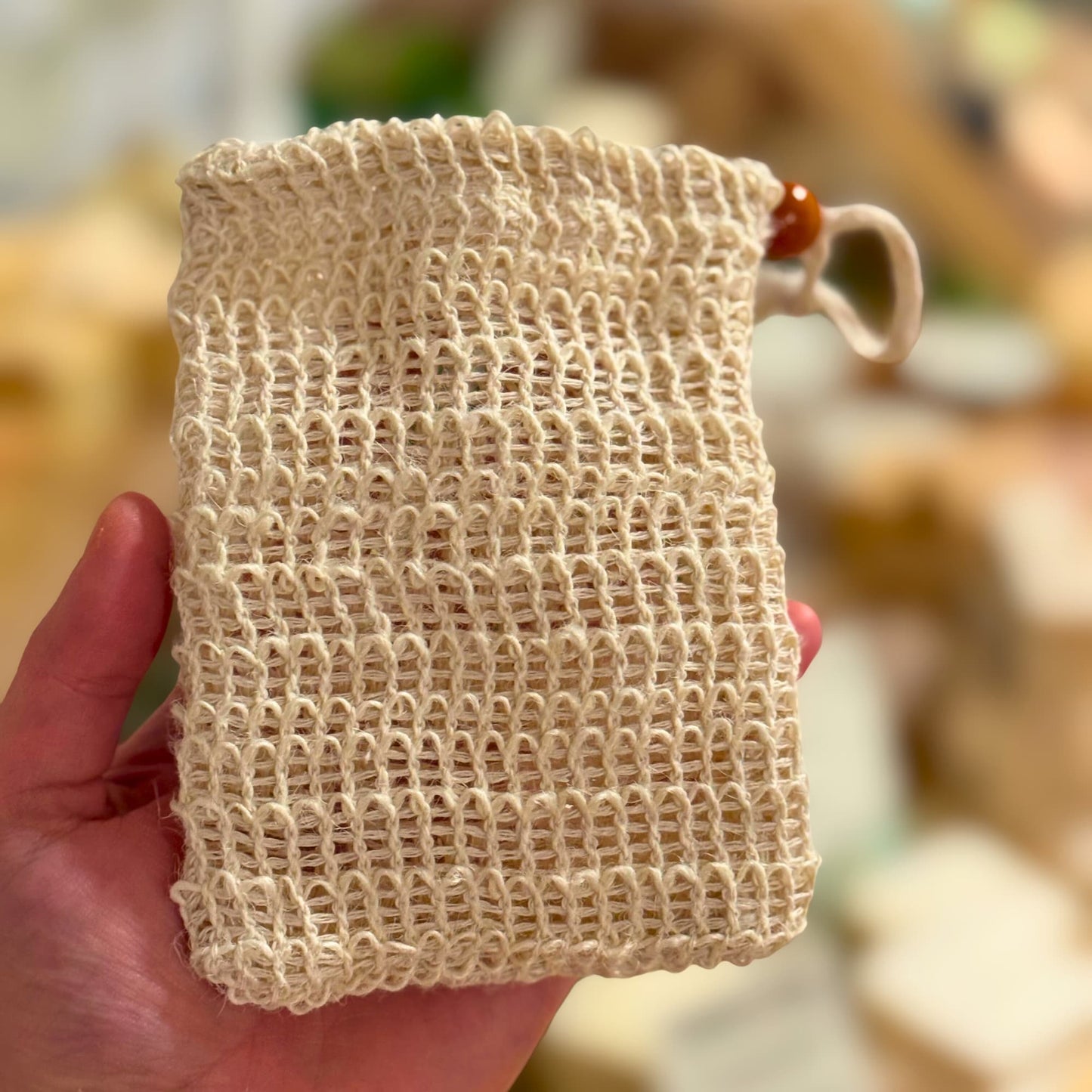 Hand holding a natural exfoliating beige woven soap bag with a blurred background