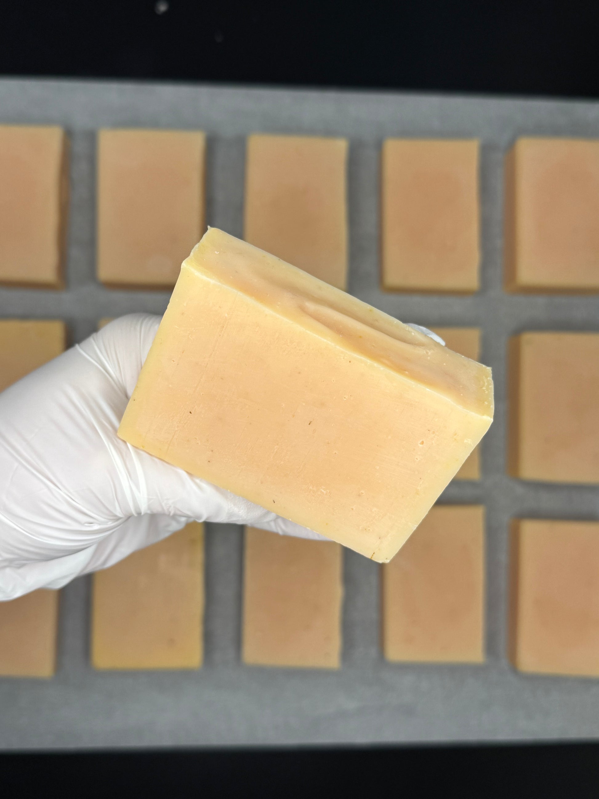 Hand holding a block of soap above a soap mold with more soap blocks.
