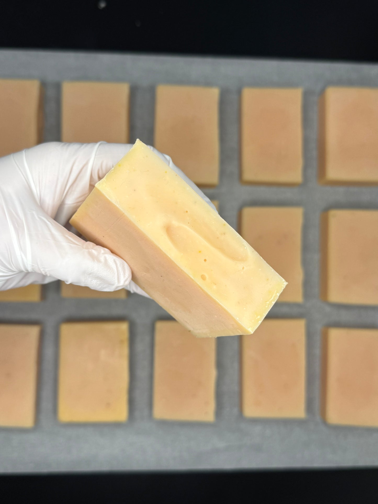 Hand holding a bar of soap above a soap mold with bars of soap in it.