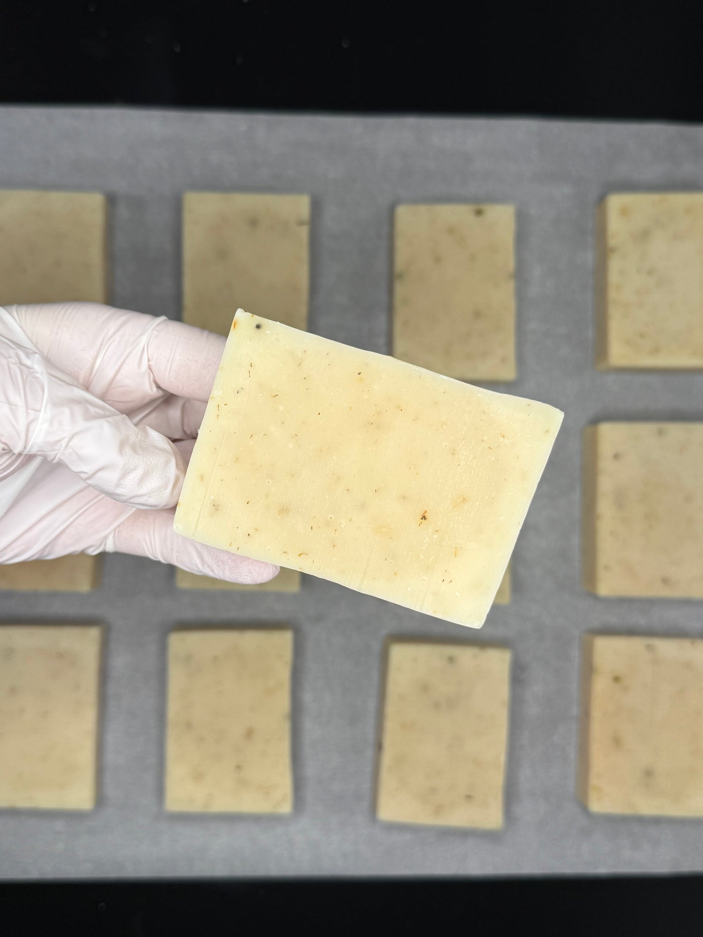 Hand wearing a glove holding a organic soap bar against a grid soap background