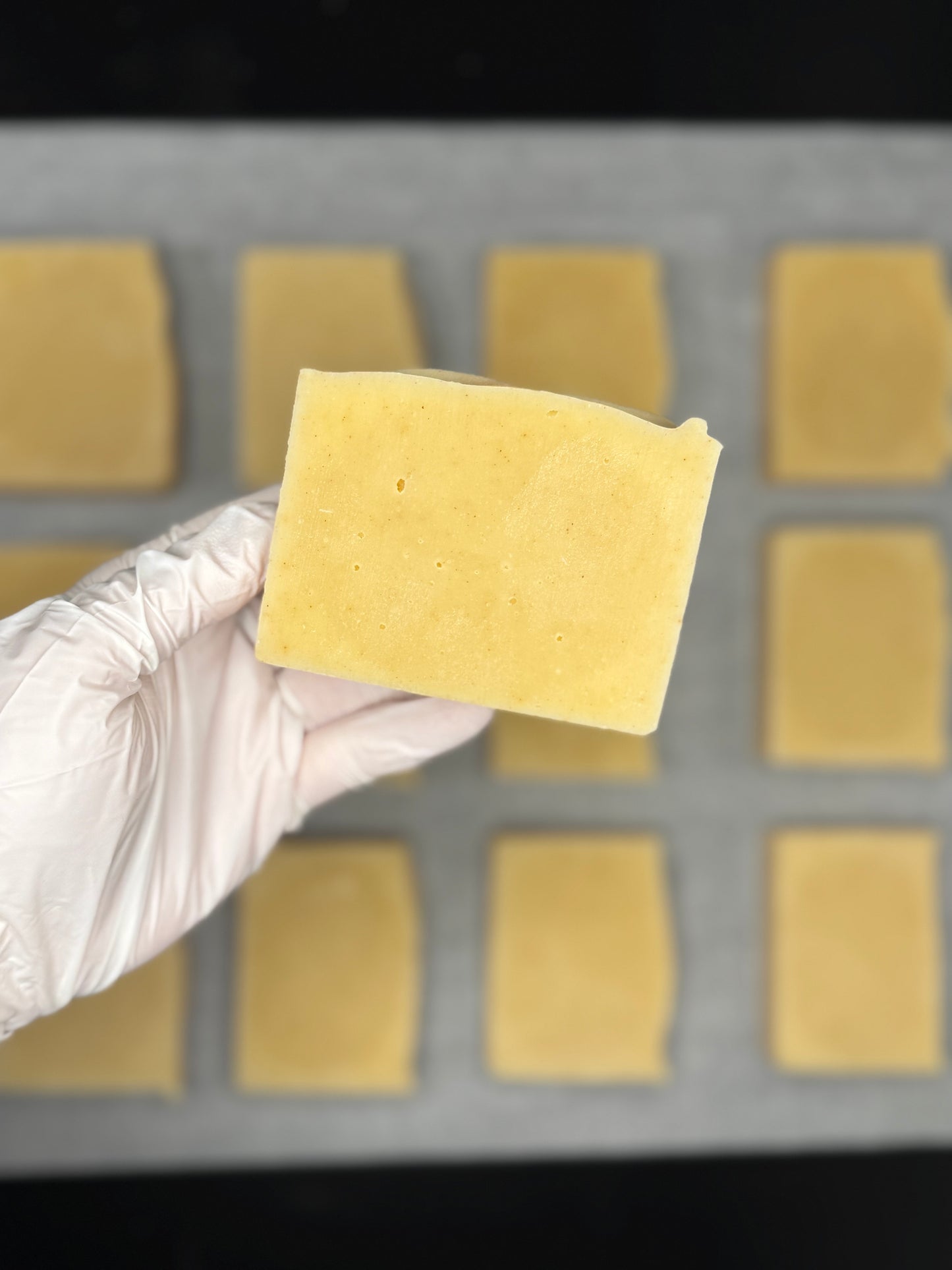 Hand wearing a white glove holding a yellow turmeric soap bar over a grid of natural turmeric soap bars