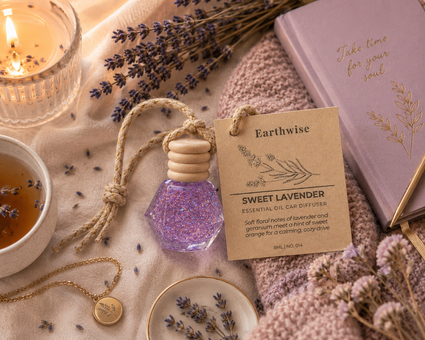 Earthwise Sweet Lavender essential oil diffuser with tag, lavender flowers, and a lit candle on a soft surface.