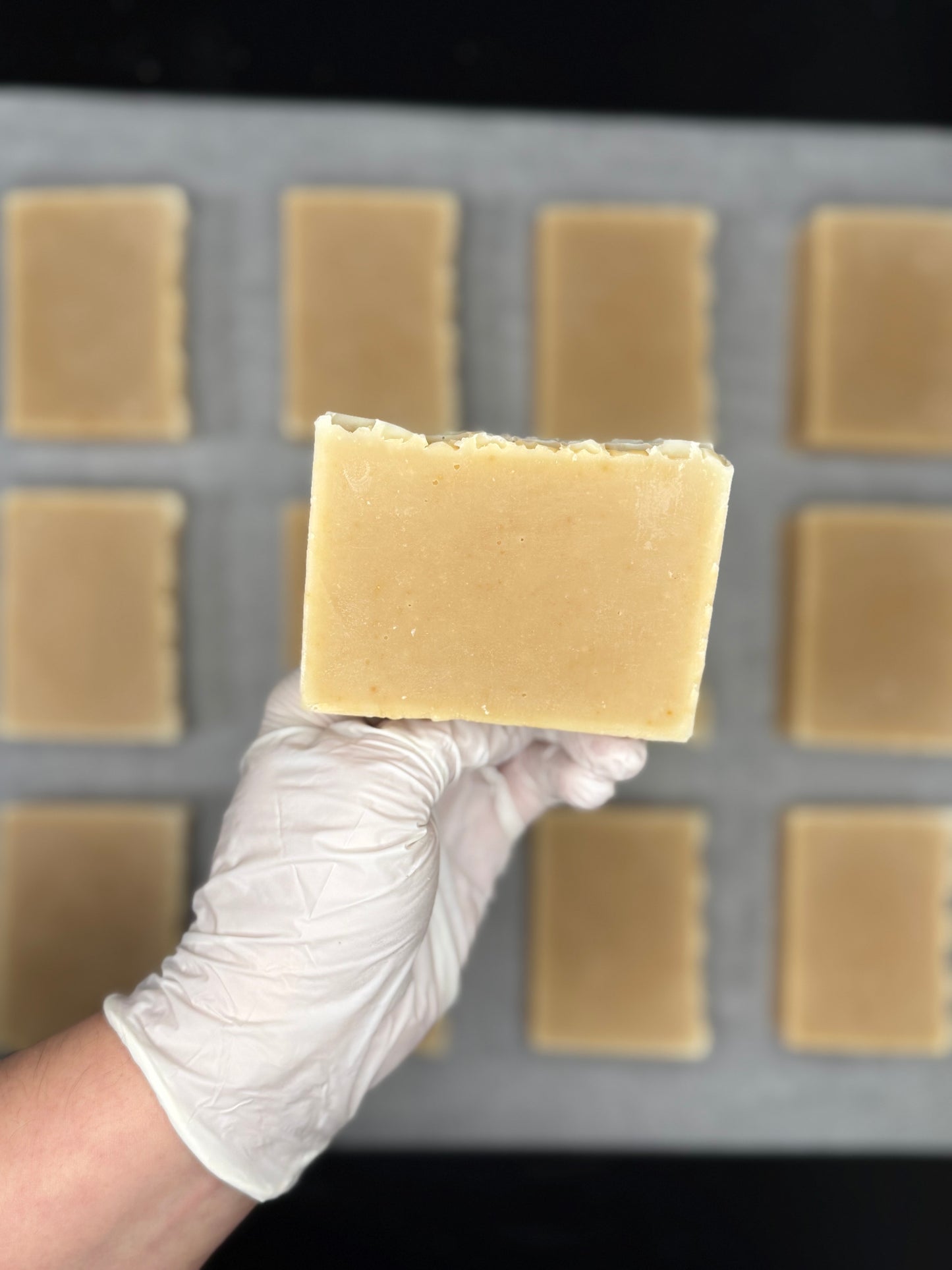 Hand holding a block of beige soap above a soap mold with more soap bars.