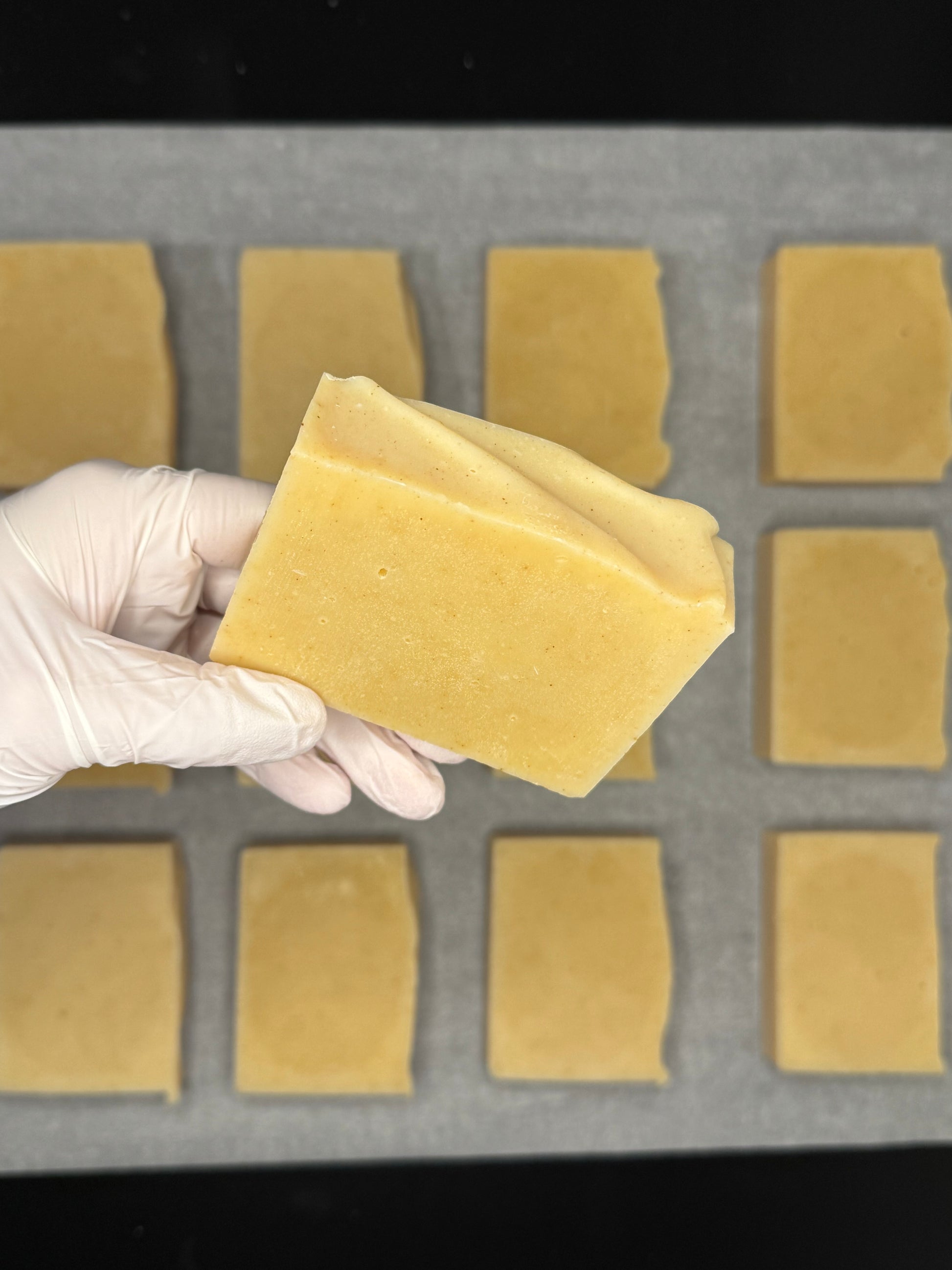 Hand wearing a white glove holding a natural turmeric soap in front of a grid of yellow turmeric soap bars