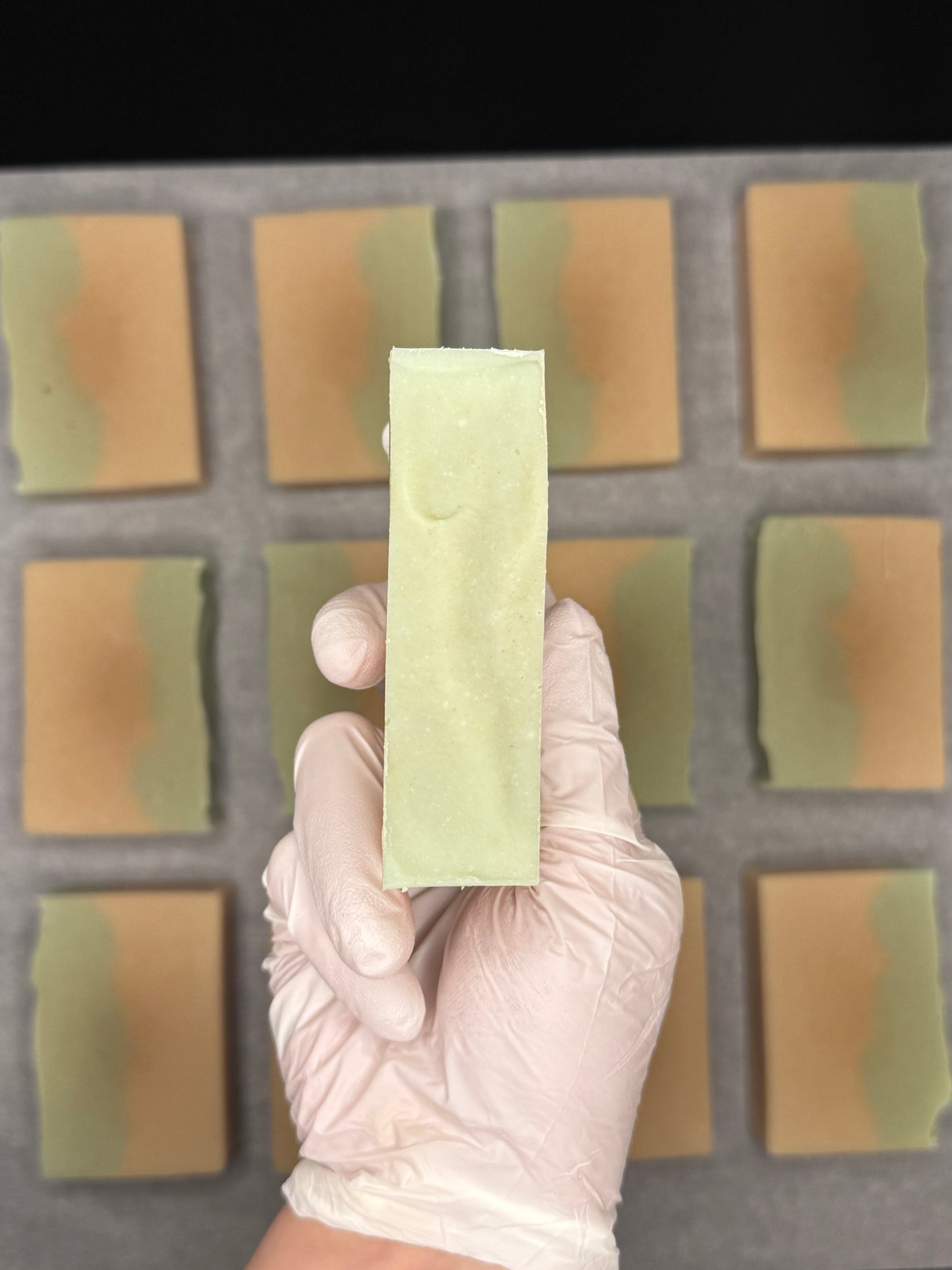 Hand holding a green soap bar in front of a grid of soap bars.