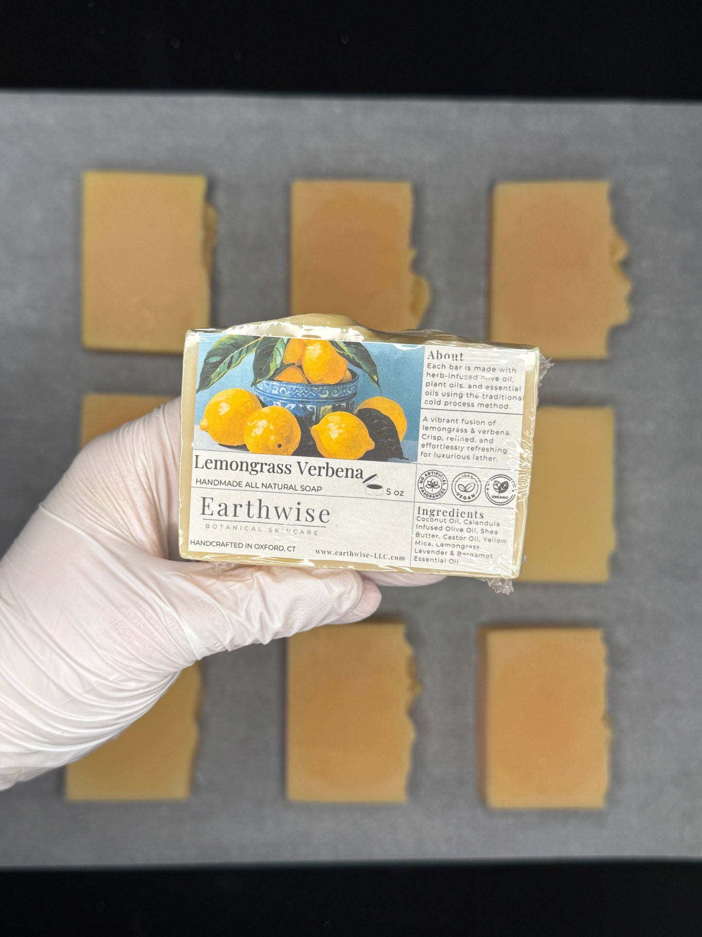 Hand holding a bar of Earthwise Lemongrass Verbena soap with soap bars in the background.