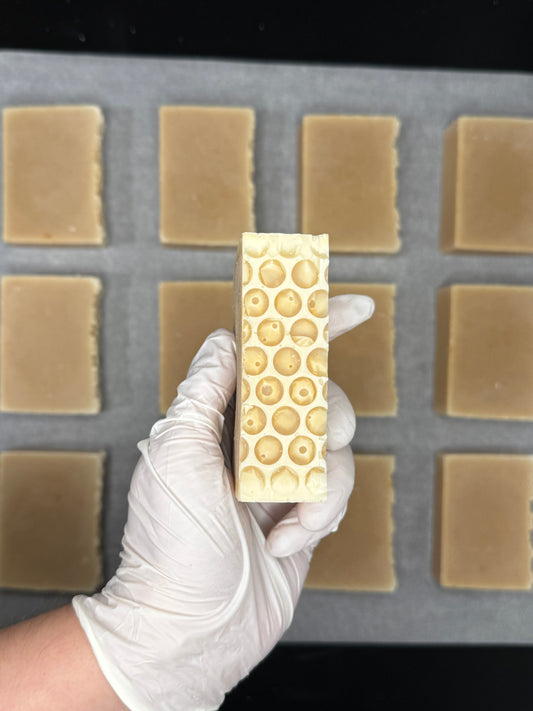Hand holding a bar of soap with a honeycomb pattern over a soap mold with bars of soap in it.