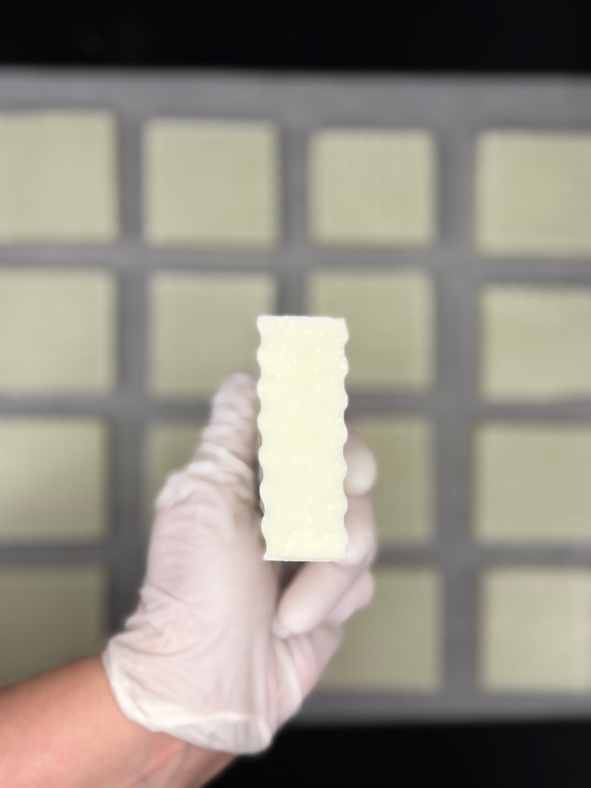 Hand wearing a white glove holding a organic sea salt soap bar against a grid background