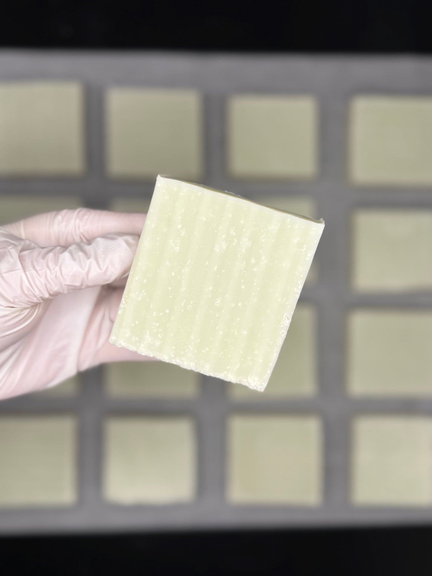 Hand wearing a glove holding a natural sea salt soap bar against a background of soap bars