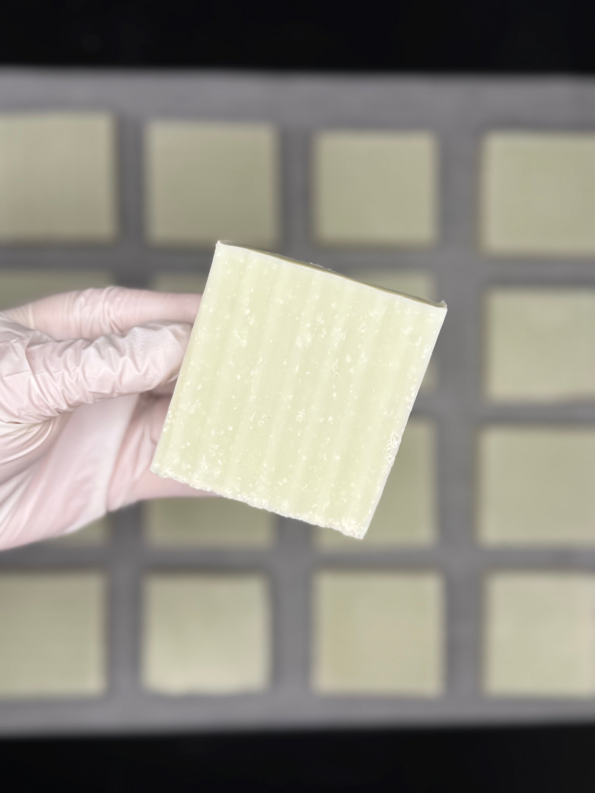 Hand wearing a glove holding a natural sea salt soap bar against a background of soap bars
