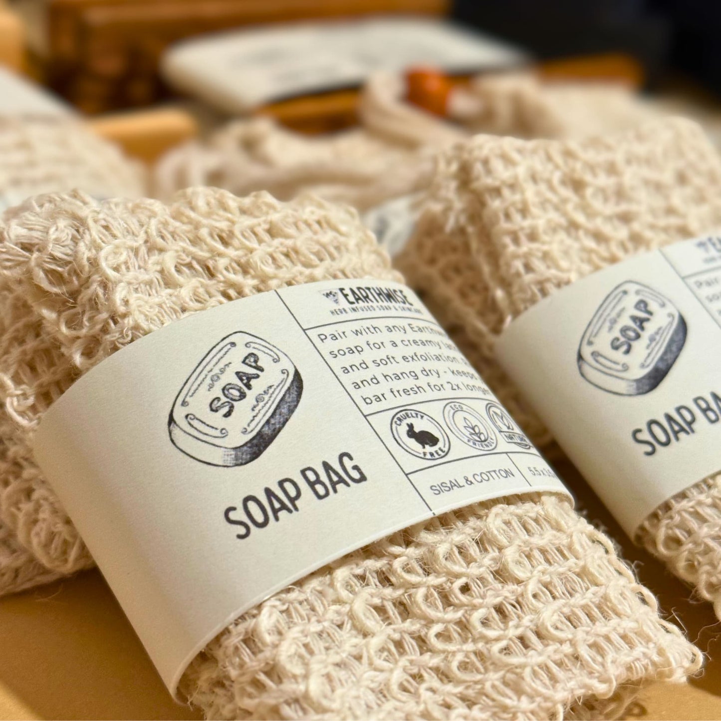 Two natural fiber soap bags with labels on a wooden surface.