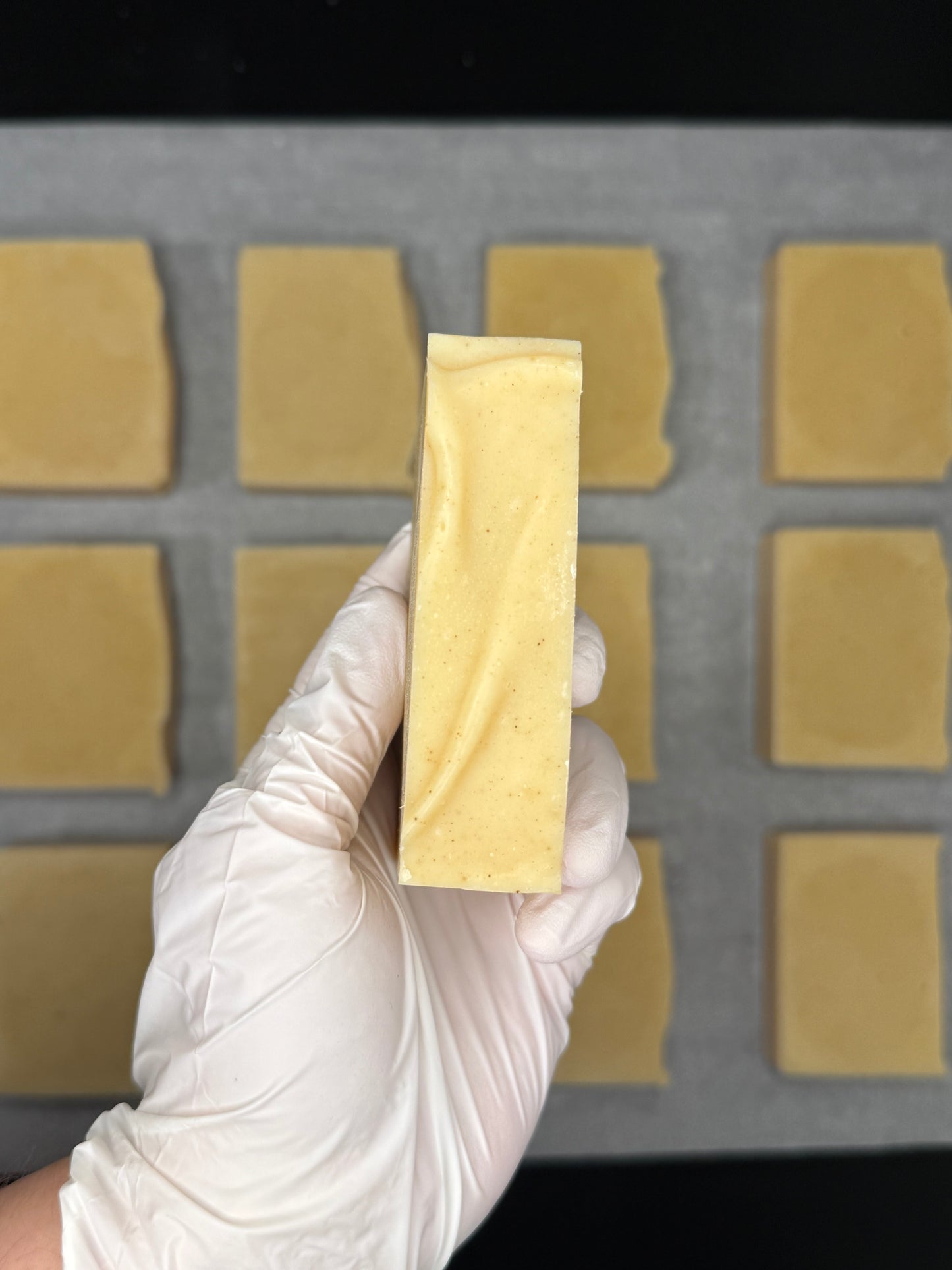 Hand wearing a white glove holding a rectangular yellow bar in front of a grid background